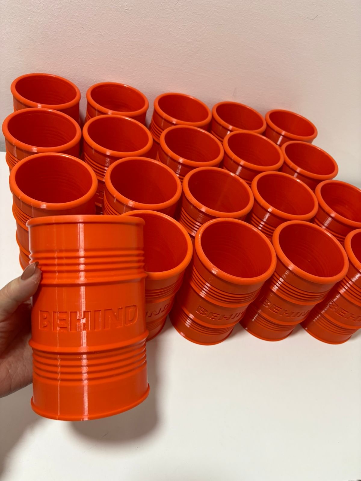 Serie de vasos naranjas con forma de barril industrial y logo Behind en relieve