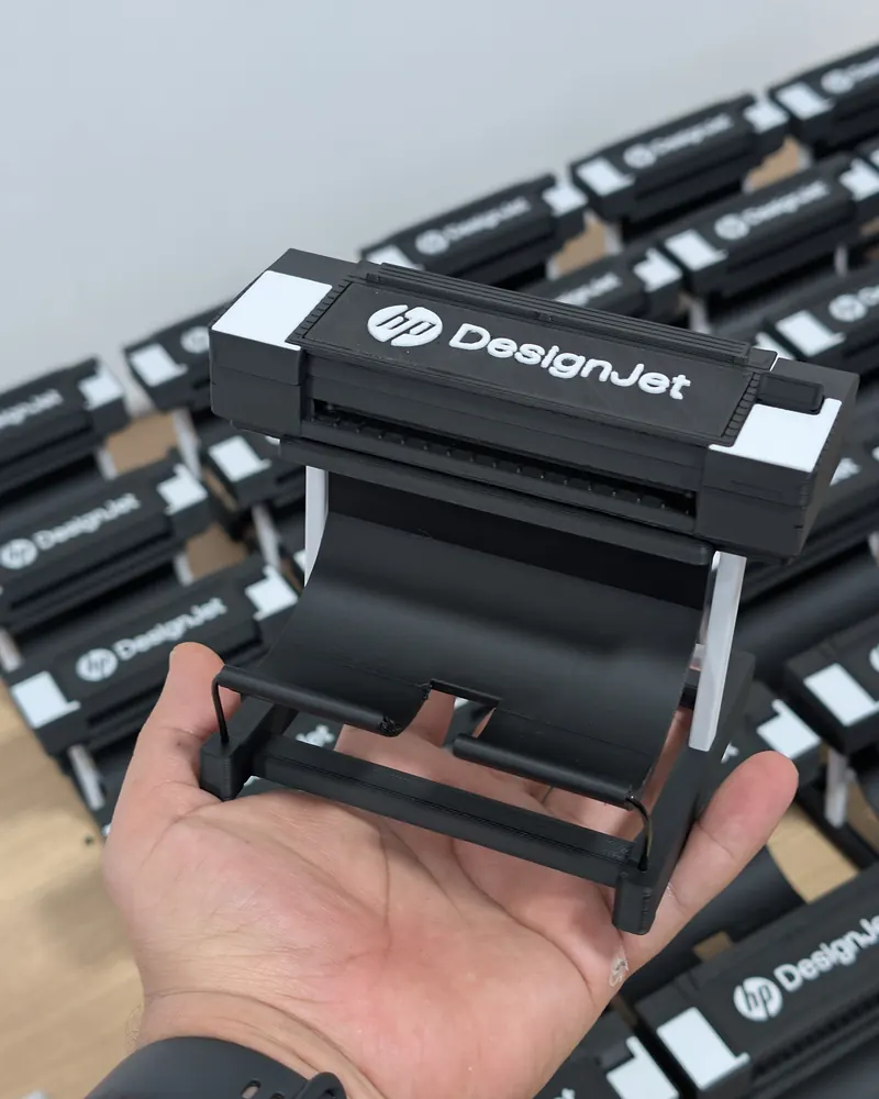 Mano sosteniendo la miniatura del plotter HP impresa en 3D, con la serie de fondo