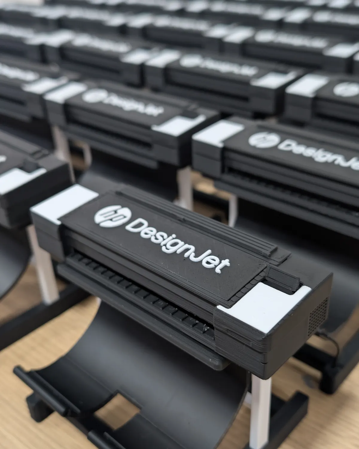 Serie de miniaturas del plotter HP DesignJet impresas en 3D, con una unidad en foco y el resto de la serie detrás